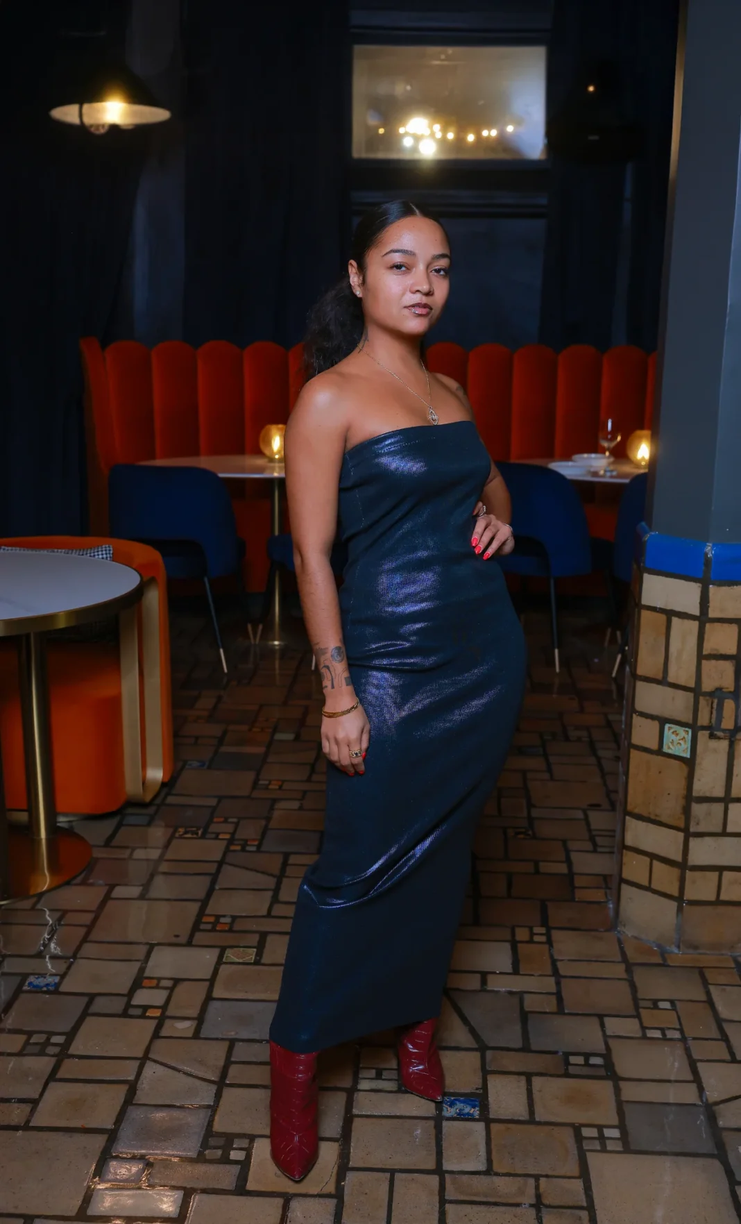 Enomah 2-21-25 Friday A stylish woman in a shimmering dress posing at Enomah in Detroit, with an upscale lounge setting in the background.