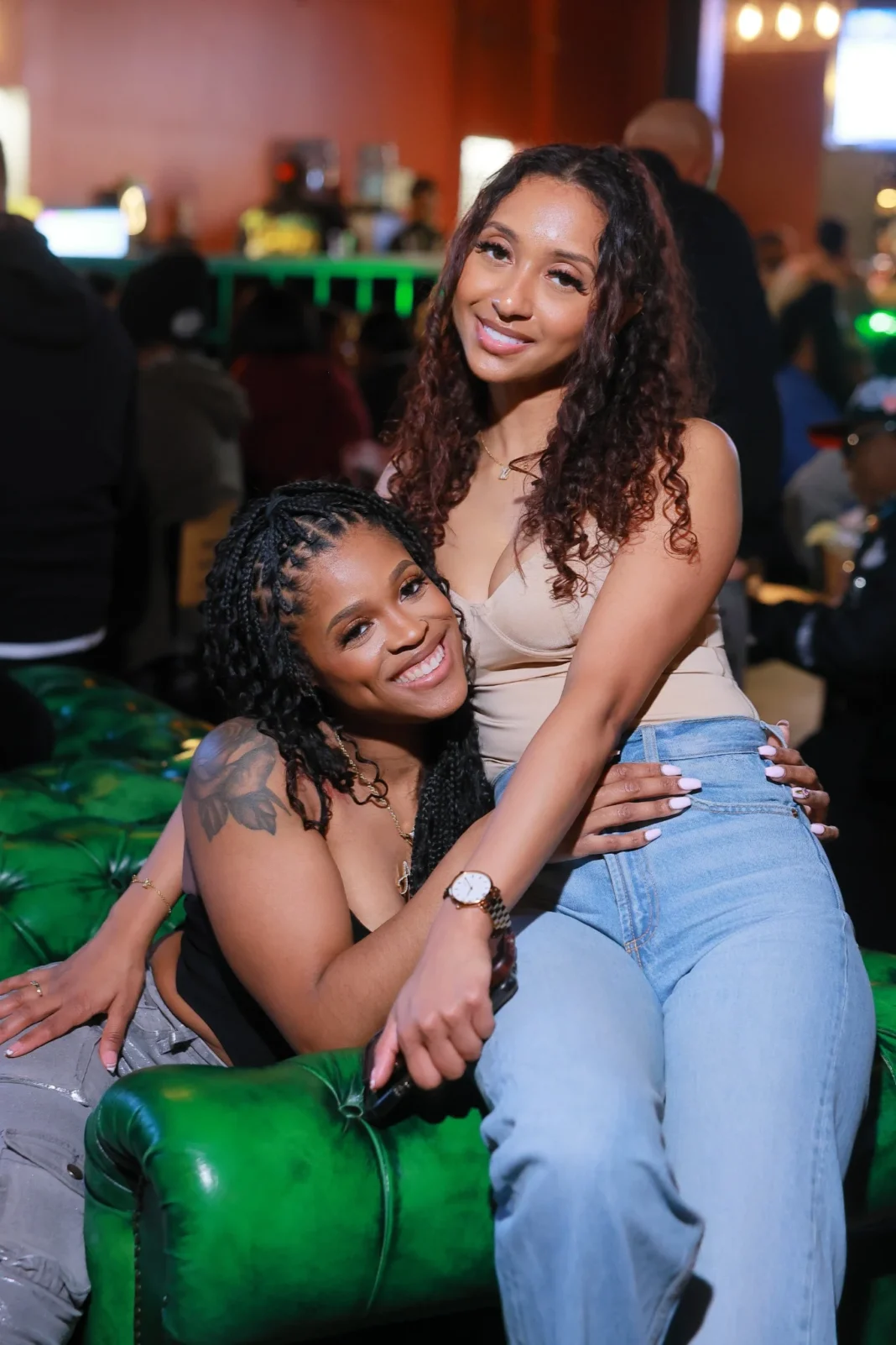 Two stylish women sharing a joyful moment at Minnie's in Detroit, with a vibrant nightlife atmosphere in the background.