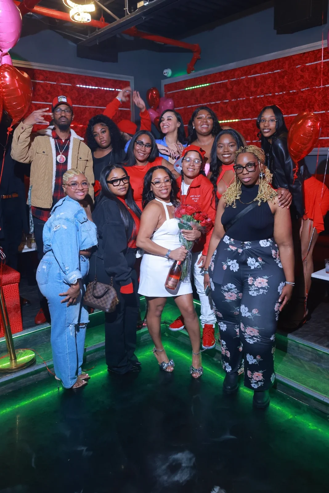A lively group posing at Preva nightclub, dressed in stylish outfits with vibrant red and black decor in the background.